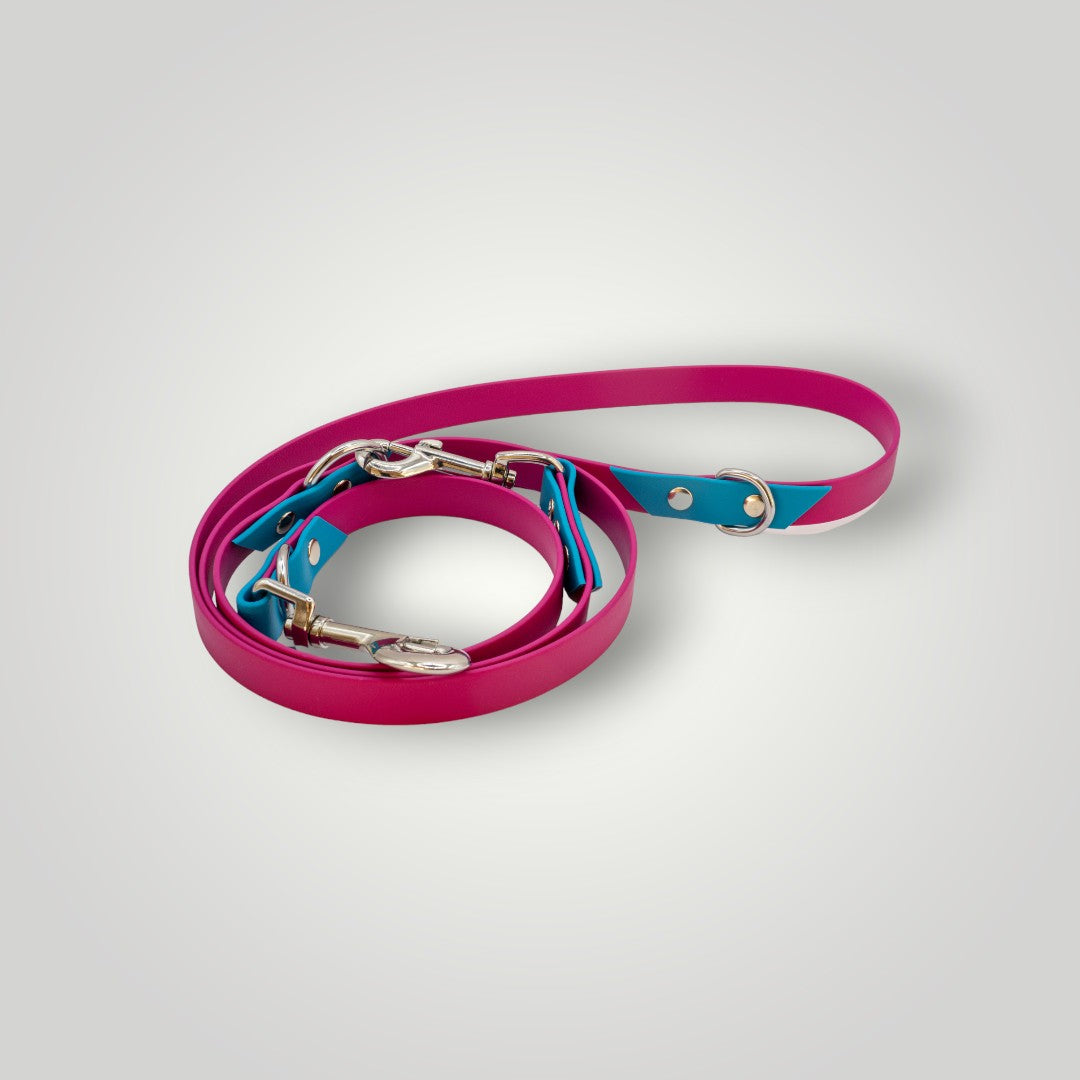 Die pfotenimglueck Biothane Hundeleine 2-fach verstellbar in Magenta-Lagune mit stylischem Design und wetterfesten Metallverschlüssen ist auf einem hellgrauen Hintergrund zusammengerollt.