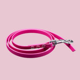 Die pfotenimglueck Biothane® Schleppleine auf Mass (genietet) ist eine leuchtend rosa, wasserabweisende Hundeleine aus Kunststoff mit Metallverschluss, ordentlich aufgerollt und auf einem schlichten hellrosa Hintergrund abgebildet.