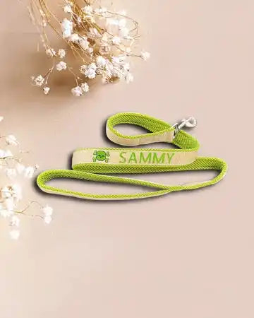 Eine grüne Hundeleine mit dem Namen „SAMMY“ und einer kleinen Hundeillustration. Die Leine ist ordentlich auf einem neutralen Hintergrund aufgerollt, begleitet von kleinen weißen Blumen in der Ecke.