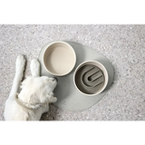 Weißer Hund liegt neben Hundenapf Cali und Hundespielzeug auf Matte, echtes Highlight