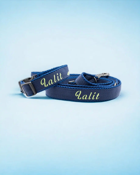 Ein blaues Set aus Hundeleine und Halsband mit der gelben Aufschrift „Lalit“. Halsband und Leine sind ordentlich aufgerollt und heben sich von einem hellblauen Hintergrund ab.