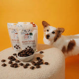 Pure bites hundespielzeug verpackung in weiß und orange mit dunkelbraunen snacks neben kleinem weißen napf