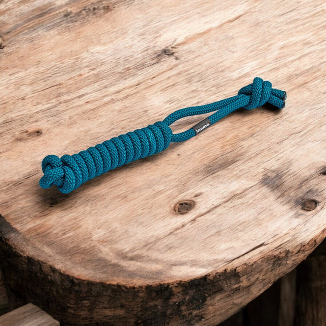 Das „pfotenimglück treusinn. Tau-Spielzeug SPIELY“ für Hunde ist ein robustes Hundespielzeug mit einem blauen Affenfaustknoten aus Paracord mit Schlaufe und Quastenende auf Holz und zeigt exquisite Handwerkskunst.